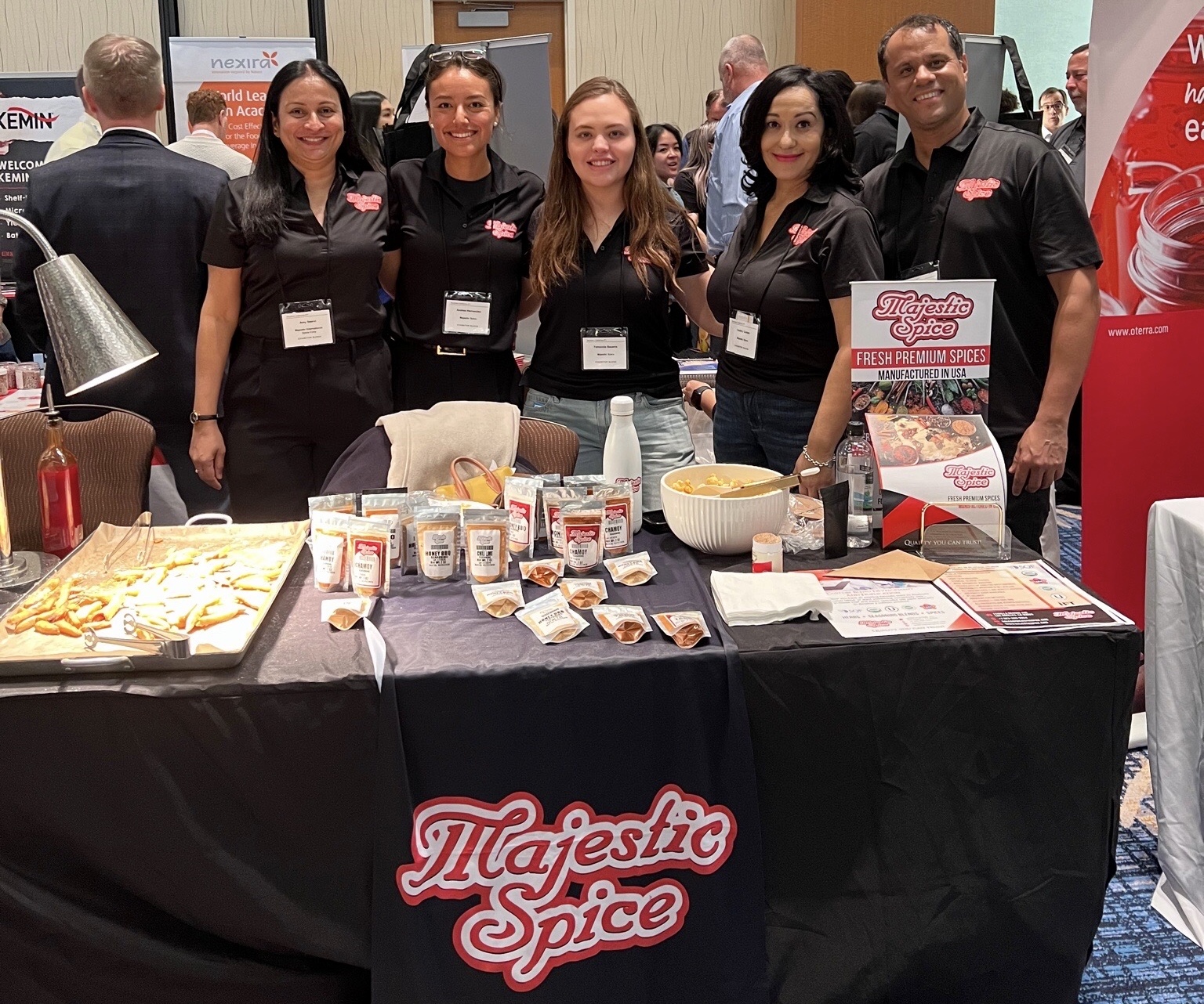 Picture of Majestic Spice's team. 4 Ladies and one Man. All wearing black, behind a black Table with the Majestic Spice logo. On the table, there are Majestic Spice samples, our flyers as well as some fries and a white bowl with chili gummies.